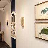 Interior of art gallery with framed pictures of green sea monster like shapes.