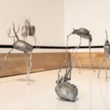Silver potato sculptures with spindly legs on a white shelf.