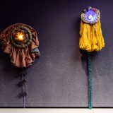 Interior of art gallery with purple wall with two sculptures with ceramic circles and fabric frills attached to it