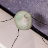 Interior of art gallery showing small sculpture with little white human face and spindly wire legs