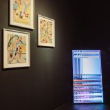 Interior of art gallery with black walls and tv propped up in the corner showing abstract colourful lines