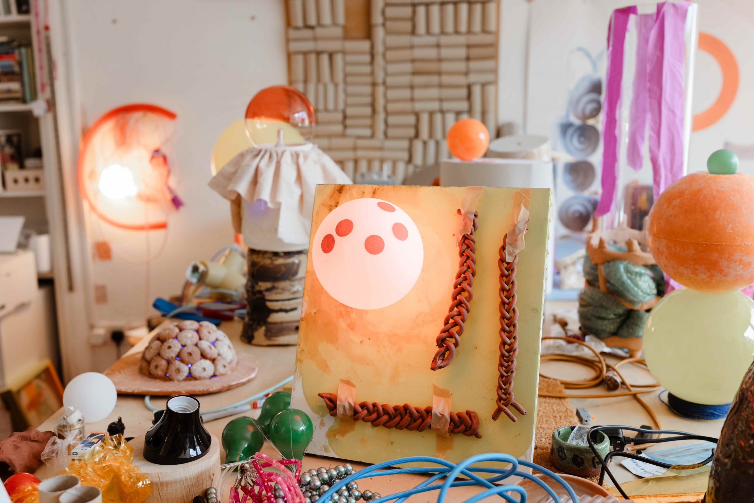 Artists studio with colourful objects on a table including globe shaped lights and plaited cords.