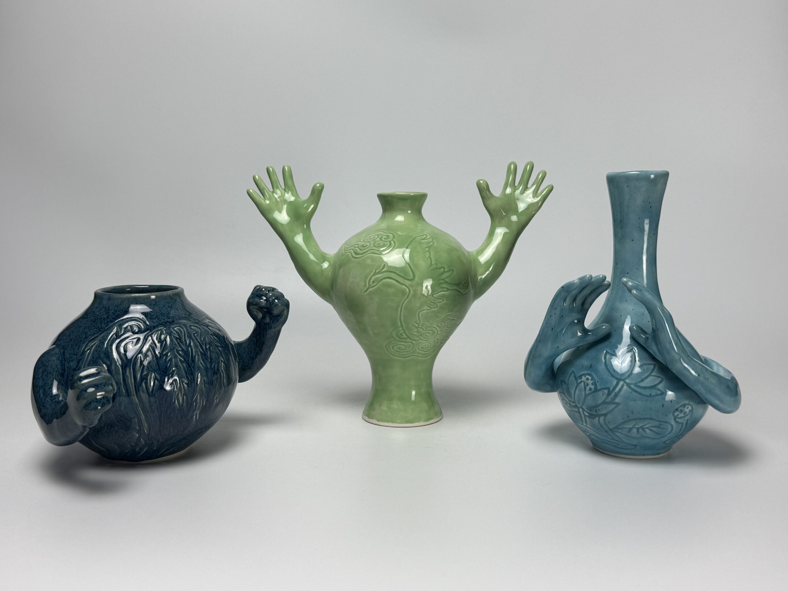 Three porcelain vases with arms which they are waving sit on a white background